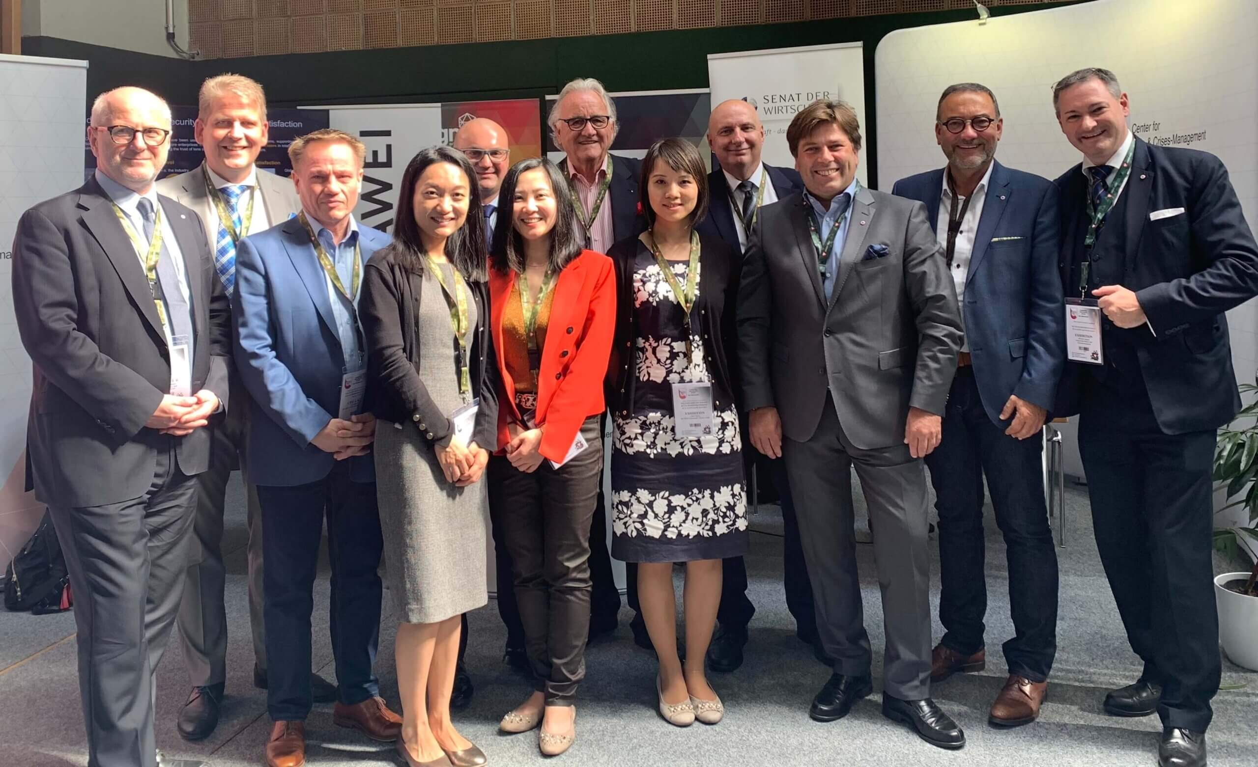 Gruppe von zehn Personen in Business-Kleidung posiert vor Bannern bei einer Konferenz oder Veranstaltung.