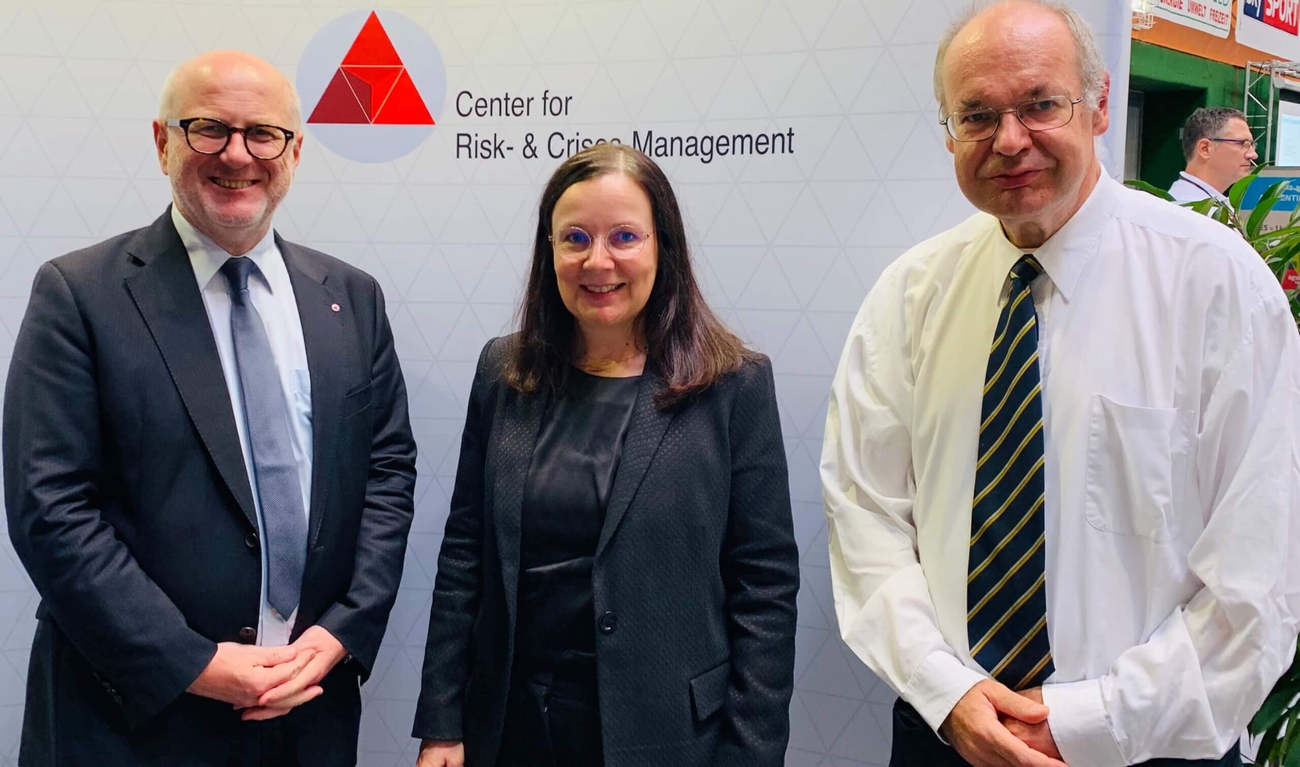 Drei Fachleute posieren vor dem Logo des Center for Risk- & Crisis Management.
