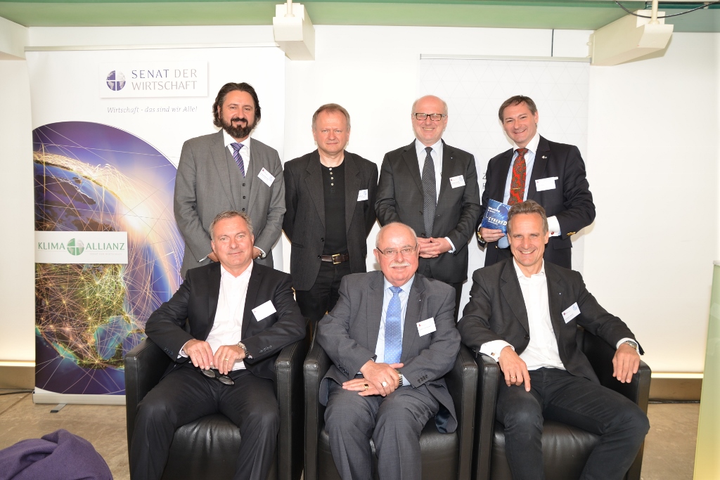 Sieben Geschäftsmänner in formaler Kleidung bei einer Veranstaltung des Senat der Wirtschaft.